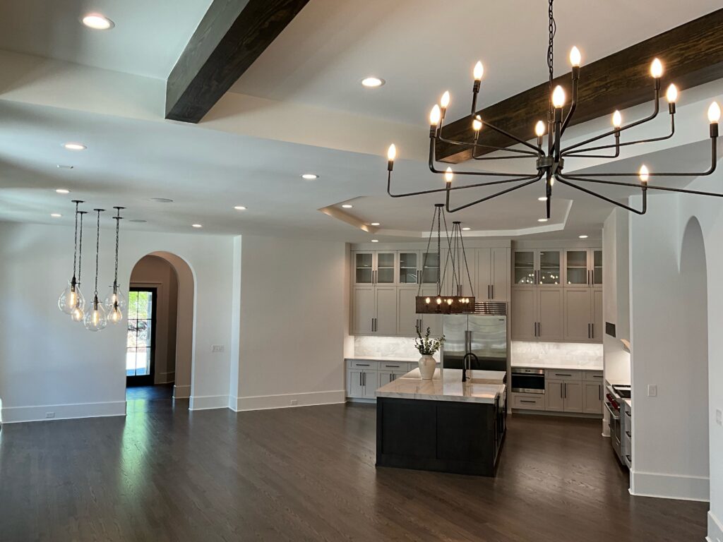 An open concept kitchen with inset lights and living room with Edison bulbs and a modern black iron chandelier hanging from the ceiling.